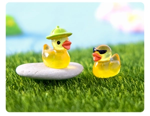 Miniature yellow luminous duck figurines with green hat and sunglasses on pebble and grass
