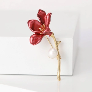 Detailed shot of red enamel magnolia brooch with gold accents and a white pearl