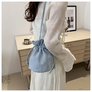 Light blue drawstring bucket bag with crinkled fabric texture worn by a model in a room