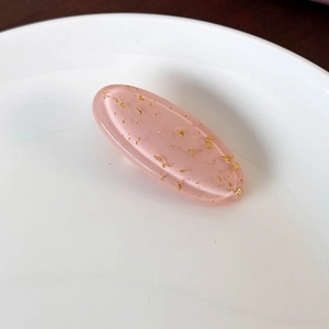 Detail of pink resin oval hair clip with gold foil flakes on a ceramic plate