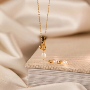 Detail of 18K gold plated necklace and pearl earrings on soft silk fabric and book