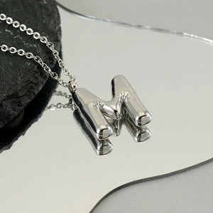 Macro view of silver chunky bubble letter M pendant on a mirror with stone detail