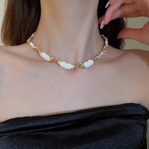Gros plan du collier vintage à maillons X dorés avec émail blanc porté par un modèle