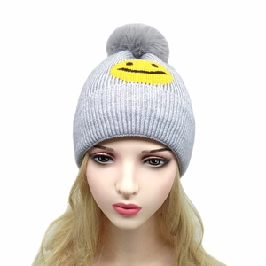 Graue Strickmütze mit großem Pelzbommel und gelber Smiley-Stickerei für den Winter
