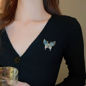 Détail d'une broche papillon plaquée or avec zircons et nacre colorée sur un pull noir