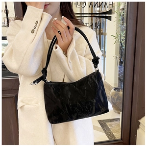 Detail of crinkled black shoulder bag featuring a large knot strap and silver zipper