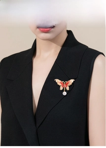 Detail of red enamel butterfly brooch with crystals and pearl drop on black blazer