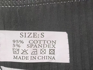 Macro shot of product care label showing S size and 95% cotton material on black rib fabric