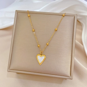 Close-up of golden heart pendant necklace with white inlay on soft silk background