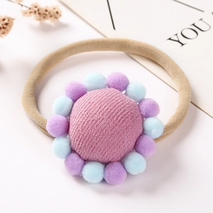 Détail d'un bandeau bébé avec fleur en tissu rose et pompons doux sur nylon