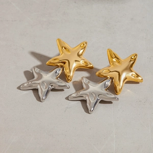Detail view of 18K gold and silver mixed textured starfish earrings on concrete