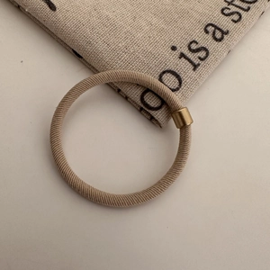 Detail of khaki high-elastic hair tie with decorative gold-tone metal bead on white surface