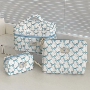 Detail view of white quilted cosmetic bag set with blue bow pattern and top handle