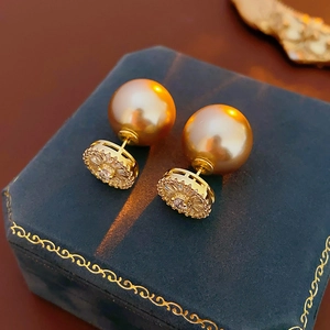 Détail de boucles d'oreilles perles dorées avec base fleurie en zircon sur écrin bleu marine
