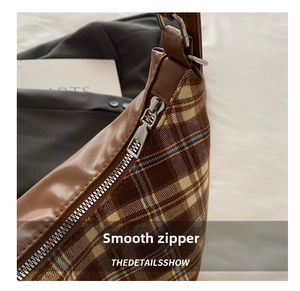 Close-up of the smooth silver metal zipper and vintage plaid fabric of the shoulder bag