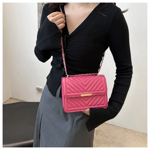 Pink quilted crossbody bag with V-shaped stitching and gold chain on model shoulder