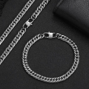 Detailed view of silver stainless steel cuban chain set on a black textured surface