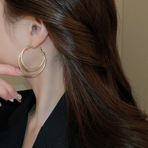 Detail of layered gold hoop earrings with twisted texture and polished finish on model