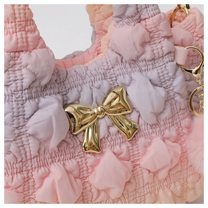 Detail of ruched cloud bag featuring a gradient purple texture and gold bow ornament