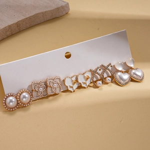 Detailed view of six pairs of gold earrings with pearls and white enamel flowers