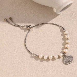 Detail of adjustable silver chain bracelet with pearl beads and shell charm on beige texture