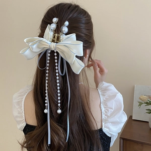 Detailed view of the large cream bow hair claw with elegant pearl tassels and blue trim