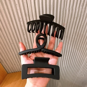 Three matte black shark hair clips held in hand, featuring large, twisted, and square designs