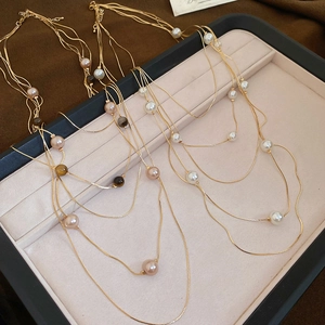 Detail of layered gold necklace with tiger eye beads and pearls on a beige jewelry tray