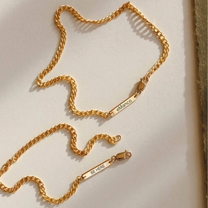Detail of gold-plated stainless steel curb chain bracelet with engraved bar pendant