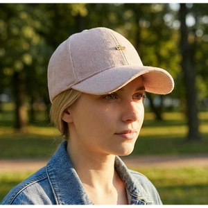 Detail of pink herringbone fabric baseball cap with small gold metal logo in nature