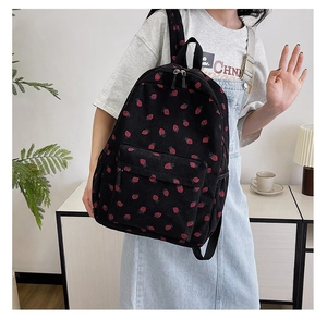 Close-up of black corduroy backpack with red strawberry print pattern and front zipper pocket