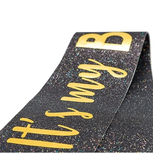 Macro shot of glittery black fabric birthday sash with gold lettering 'It's my B'