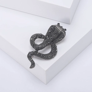 Detailed close-up of retro silver-tone snake brooch with grey rhinestones on a white pedestal