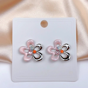 Macro detail of pink floral earrings with colorful rhinestones on a satin background