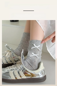 Close-up of gray knitted crew socks with decorative white ribbon bows and ribbed cuffs