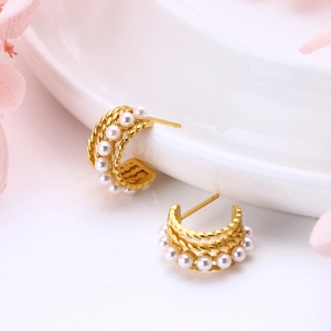Macro view of C-shaped twisted gold earrings with neat white pearls on a ceramic plate