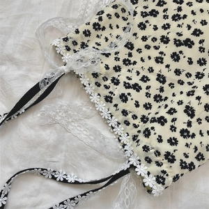Close-up of floral canvas bag featuring black daisy patterns and white lace trim detail