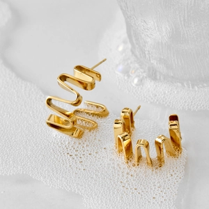 Schicke goldene unregelmäßige Wellenohrringe mit Metallic-Finish auf weißem Schaum