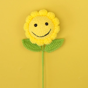 Vue détaillée d'un tournesol tricoté à la main avec visage souriant sur fond jaune uni