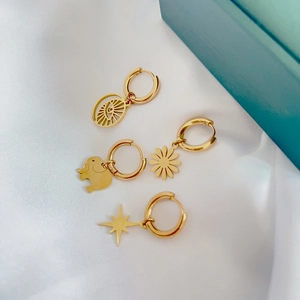 Detail of 18K gold stainless steel earrings with star and evil eye charms on white silk