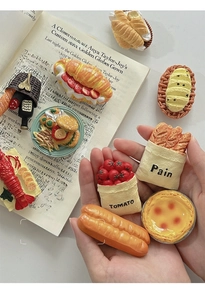 Detail of 3D resin food magnets showing realistic bread and tomato textures on a book