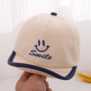 Gros plan sur casquette bébé beige avec broderie sourire bleue et bord roulé