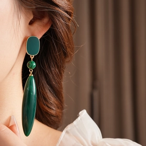 Close-up of model wearing gold-toned earrings with green malachite teardrop pendants