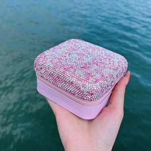 Pink jewelry box with rhinestone lid and zipper closure shown against water