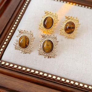 Macro detail of vintage gold square earrings featuring brown tiger eye stones on wood
