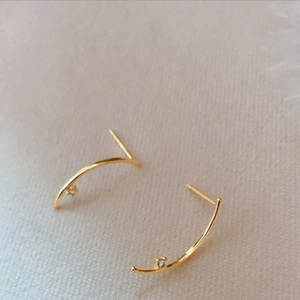 Minimalist gold curved earrings featuring small zircon accents on a soft beige background