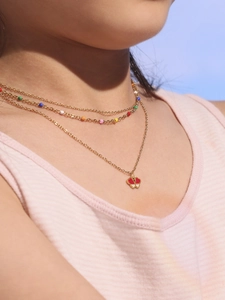 Gros plan d'un collier papillon doré à trois rangs avec perles et pendentif trèfle
