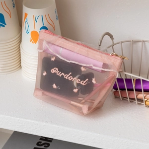 Detail of pink mesh makeup bag featuring wave embroidery and a metal zipper closure