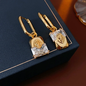Macro shot of gold-plated lion head earrings with rectangular crystal detail on navy box