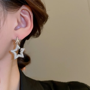 Close-up of star-shaped silver earrings with zircon crystals worn by a model